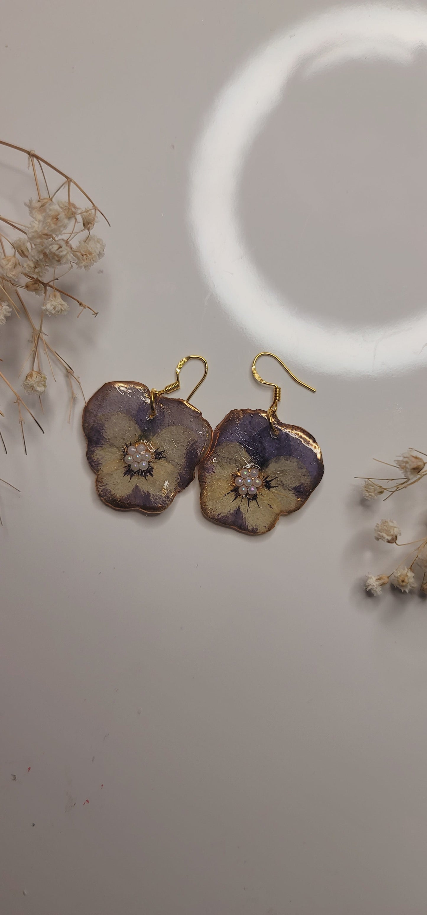 Floral earrings with gold hooks on a light gray background with dried flowers.