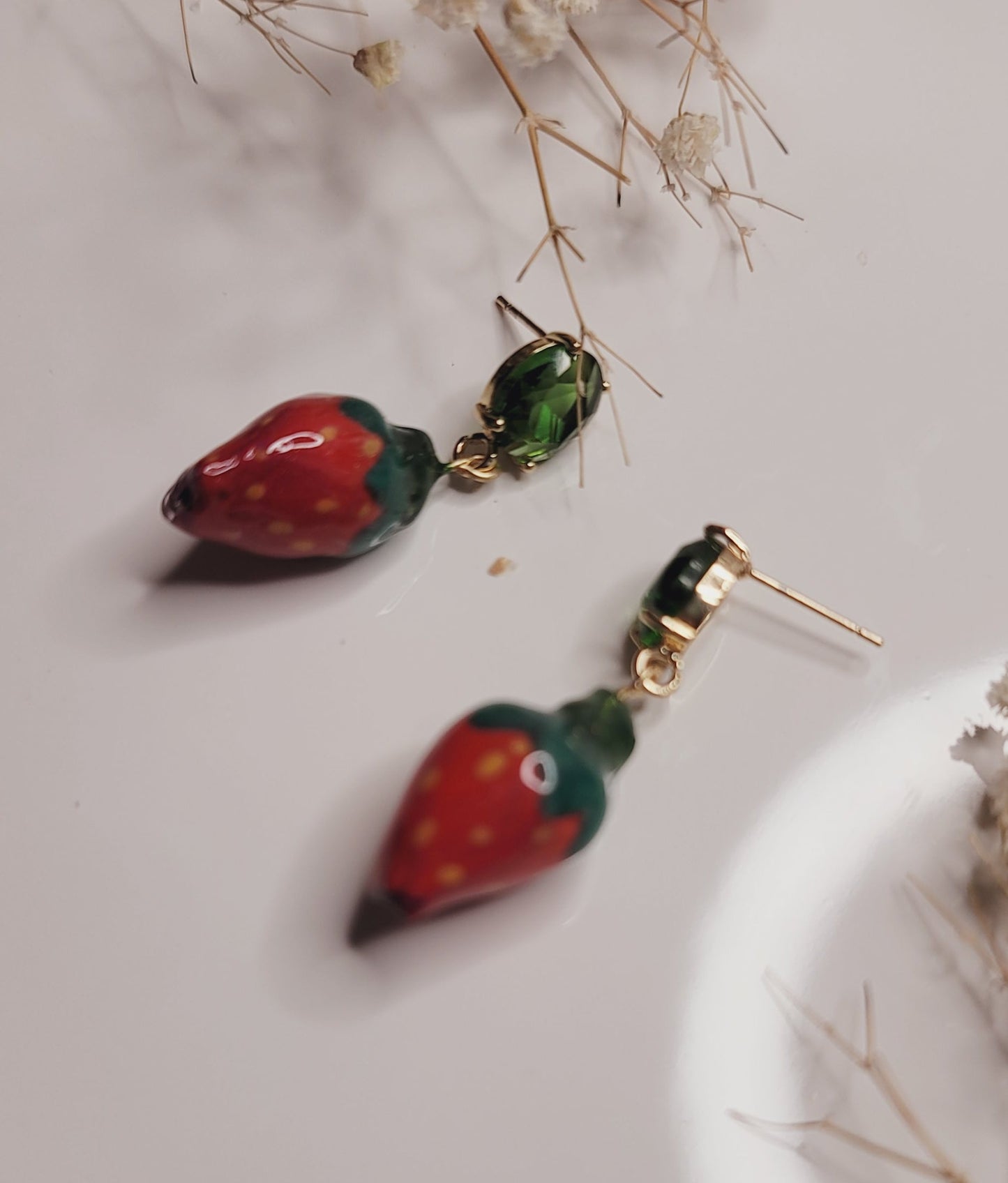 Pair of strawberry-shaped earrings on a light surface with dried flowers.