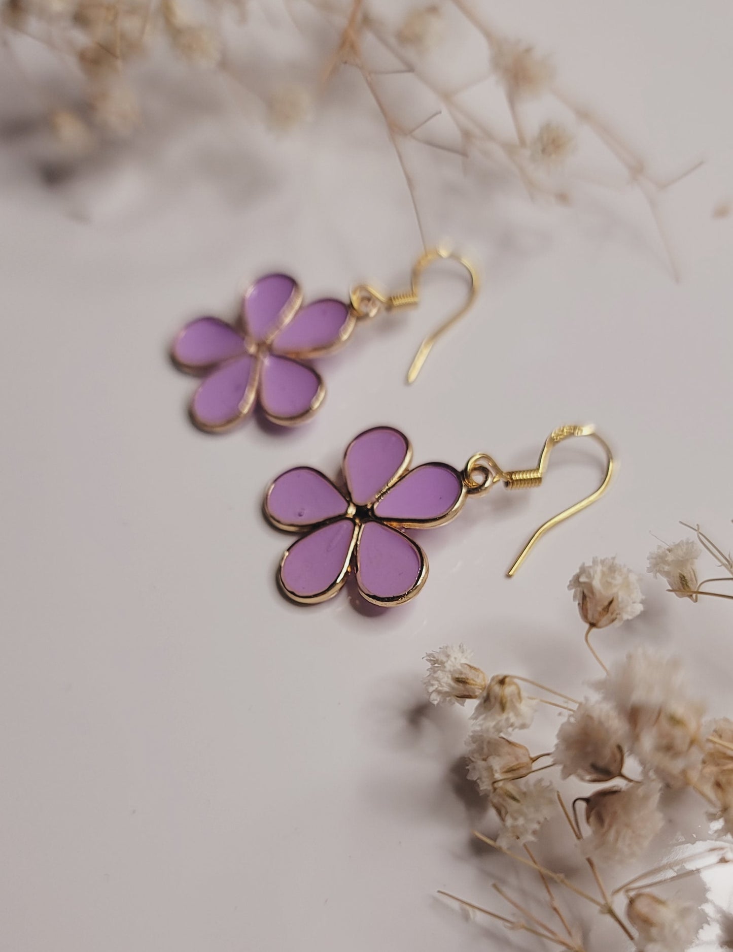 Purple flower-shaped earrings on a light background with dried flowers.