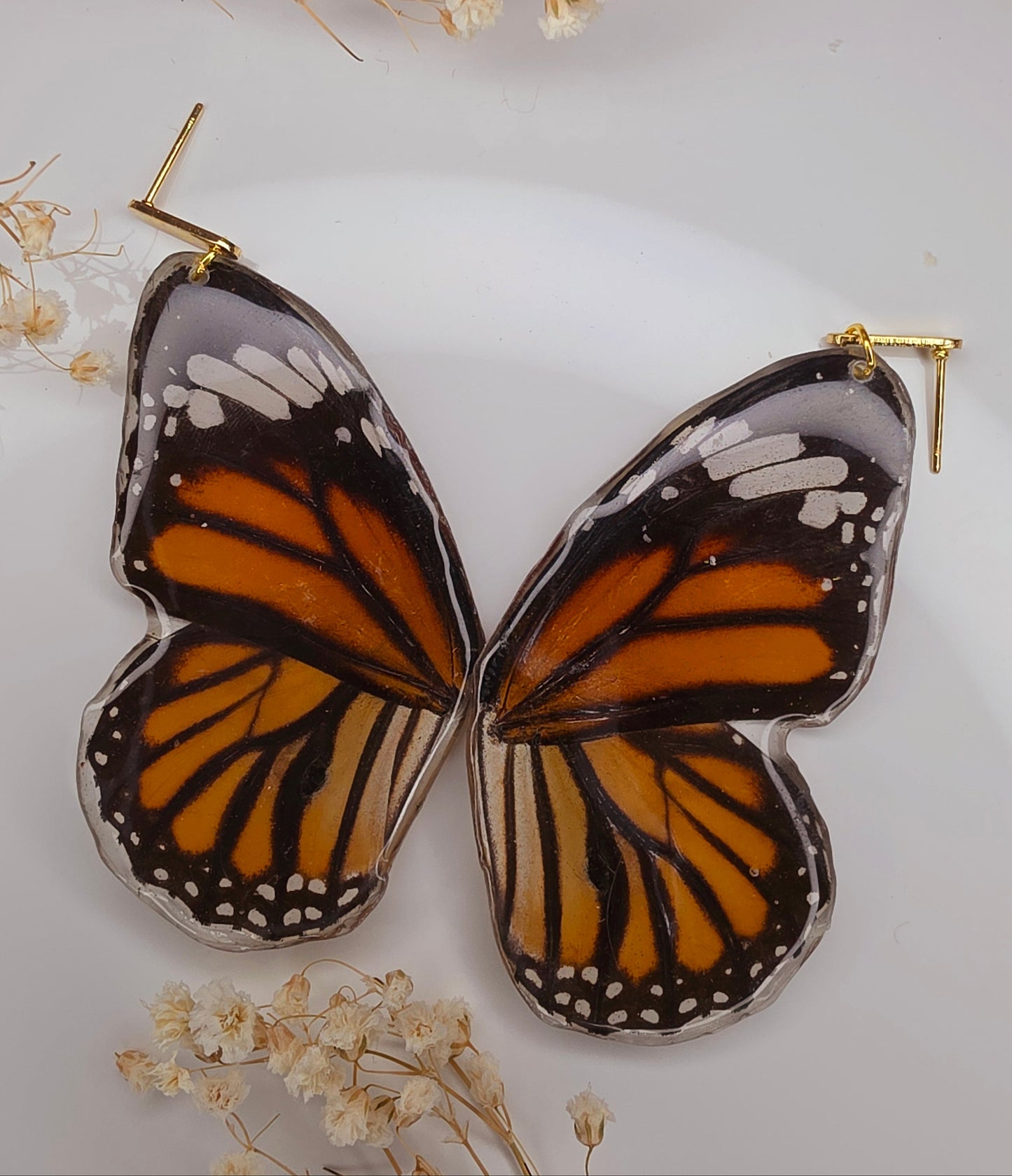 Butterfly-shaped earrings with orange and black wings on a white background with dried flowers.