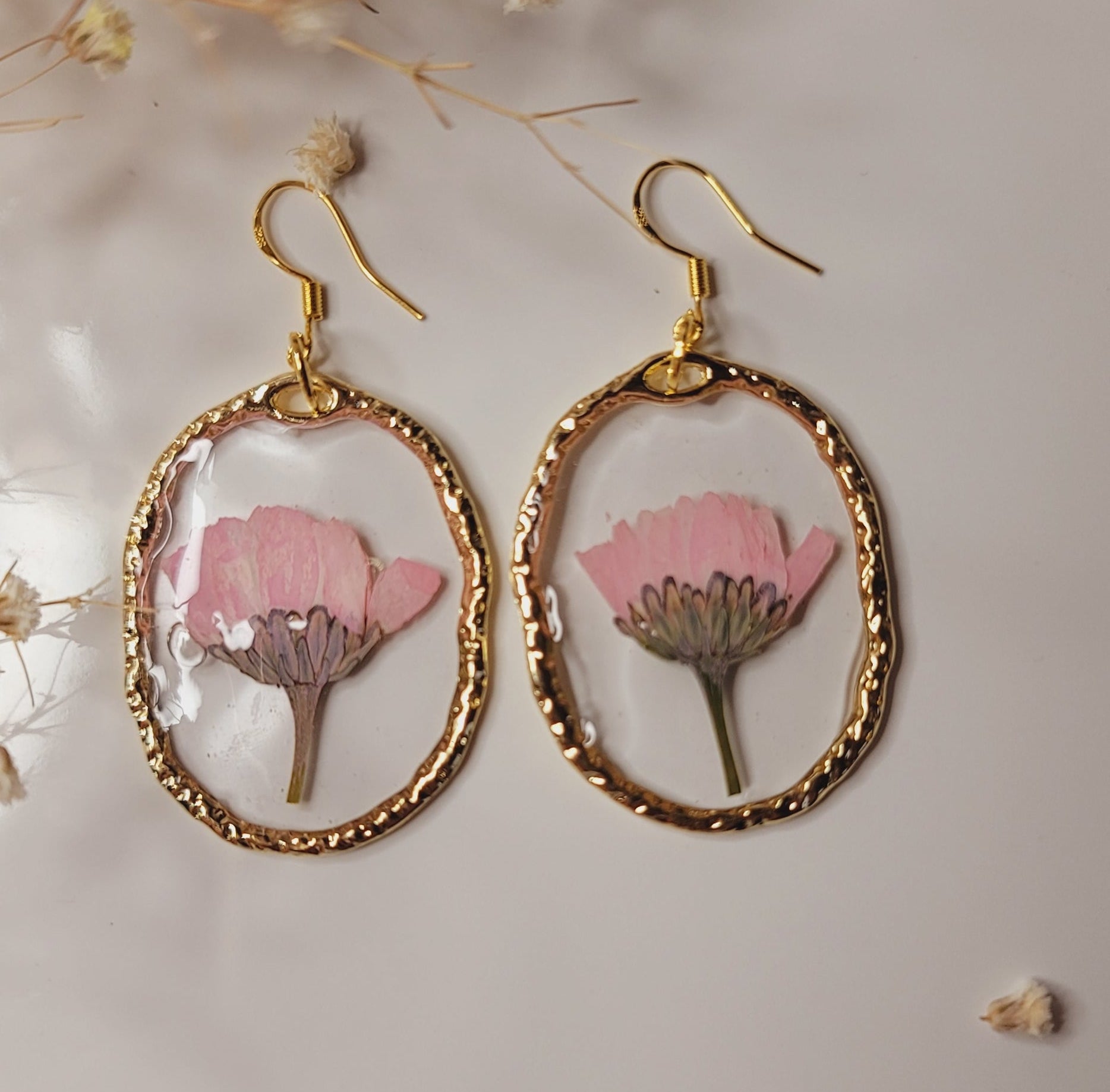 Gold-framed earrings with pink floral design on a light background
