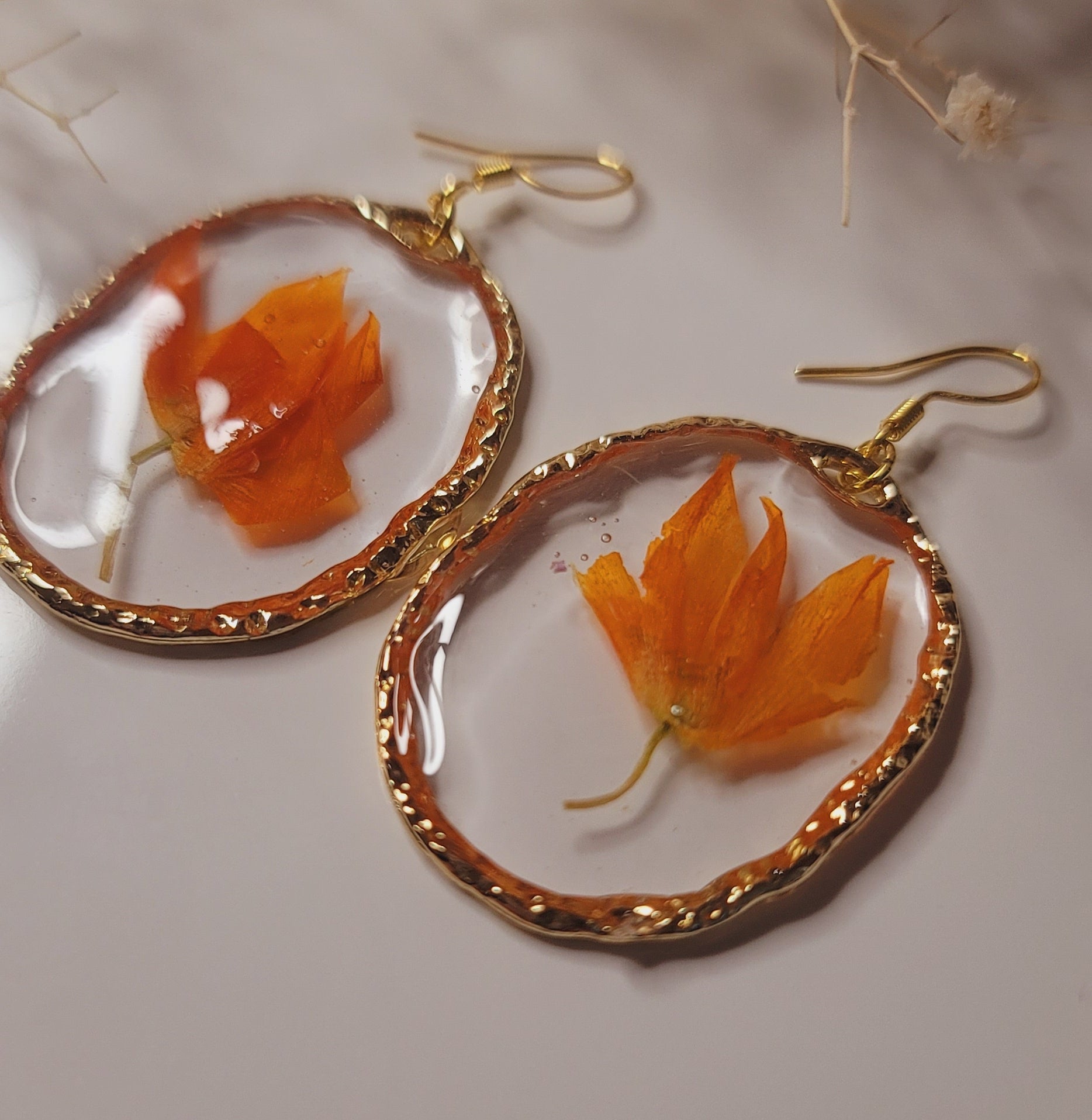 Pair of earrings with orange floral designs on a neutral background