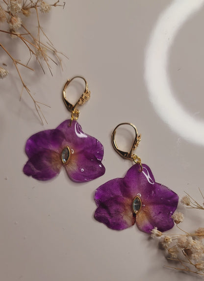 Purple flower-shaped earrings on a neutral background with dried flowers.