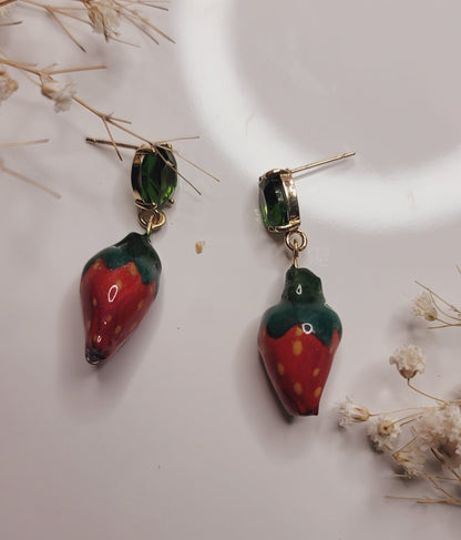 Strawberry-shaped earrings on a white surface with dried flowers.