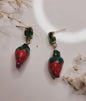 Strawberry-shaped earrings on a white surface with dried flowers.