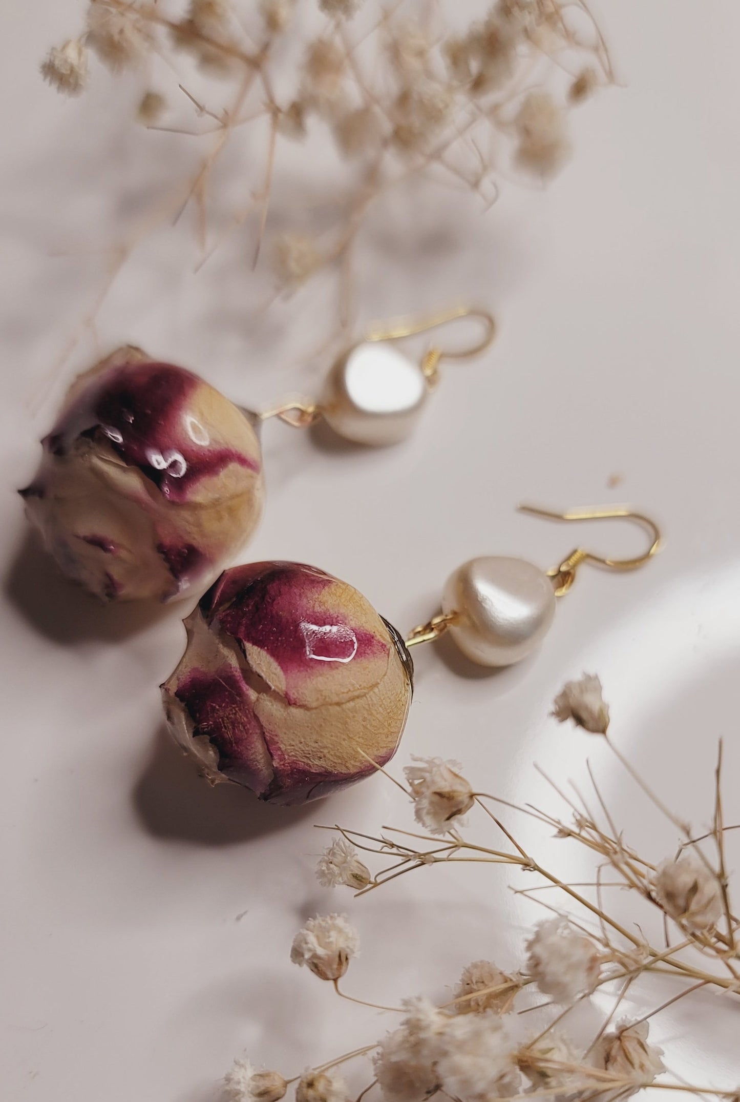 Pair of floral earrings on a soft white background with dried flowers. 