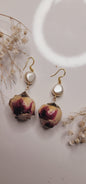 Rose petal earrings with pearl accents on a white surface with dried flowers.