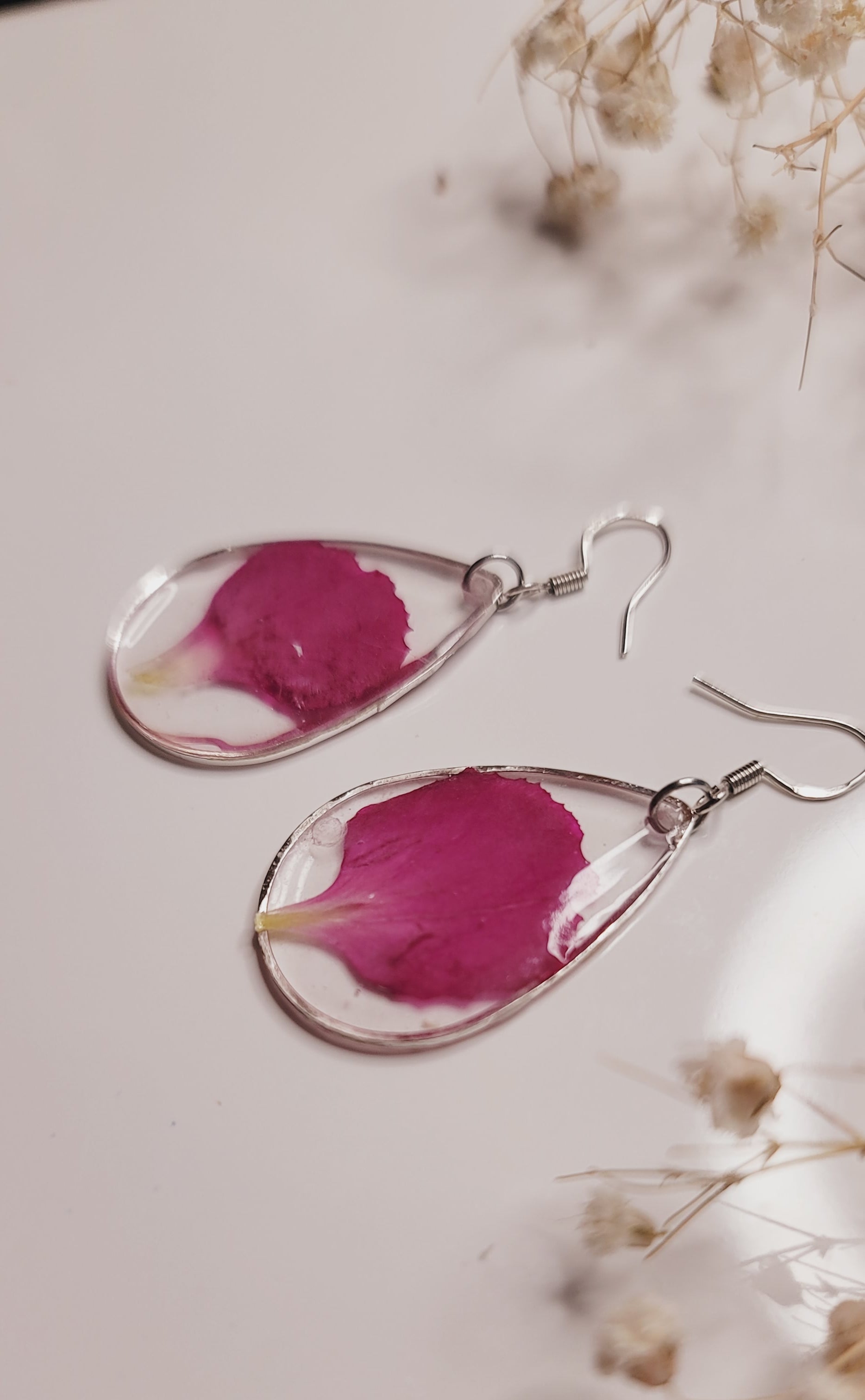 Teardrop-shaped earrings with pink floral petals on a light background