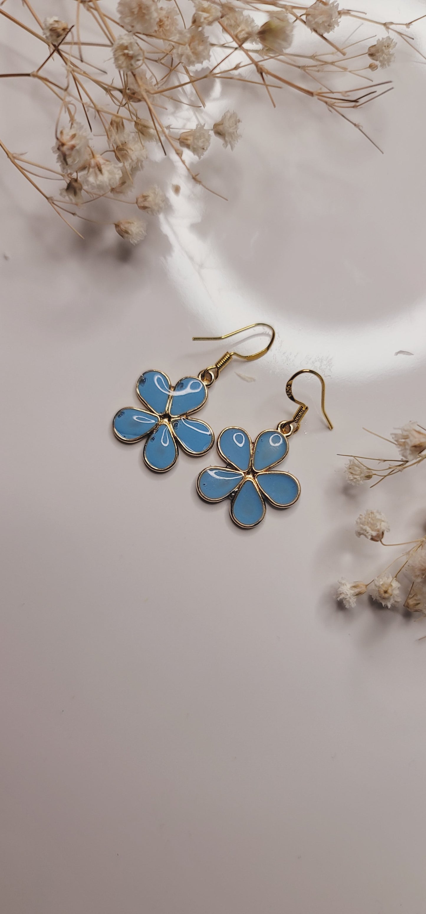 Blue flower-shaped earrings on a light background with dried flowers.