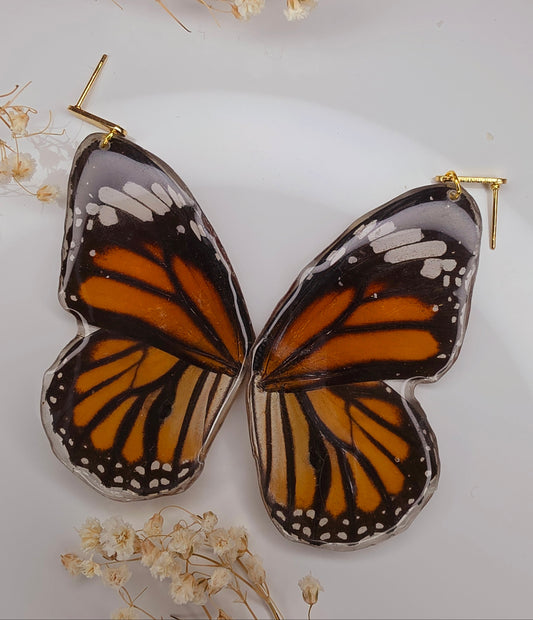Butterfly-shaped earrings with orange and black wings on a white background with dried flowers.