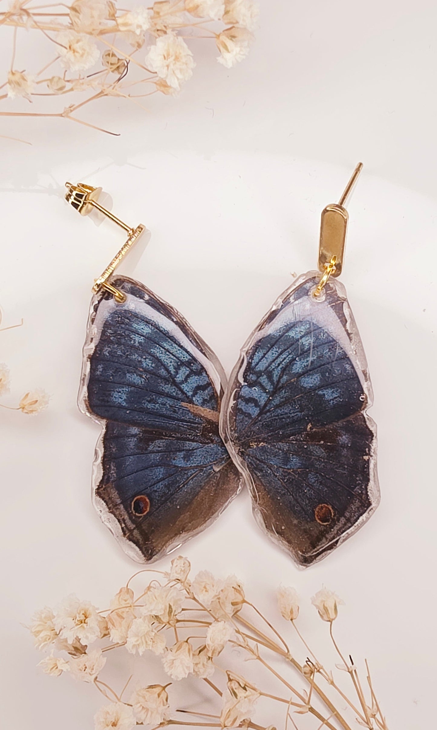 Butterfly-shaped earrings with dried flowers on a light background