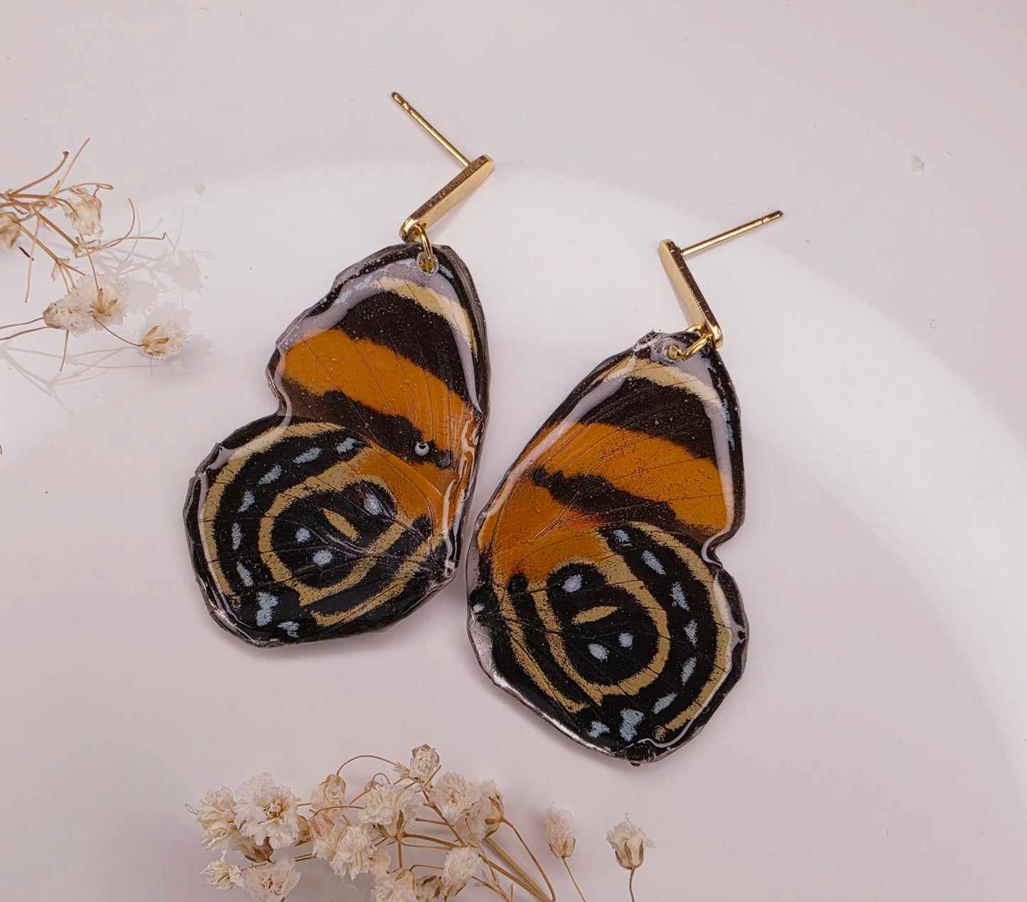 Heart-shaped earrings with butterfly design on a white background with dried flowers.